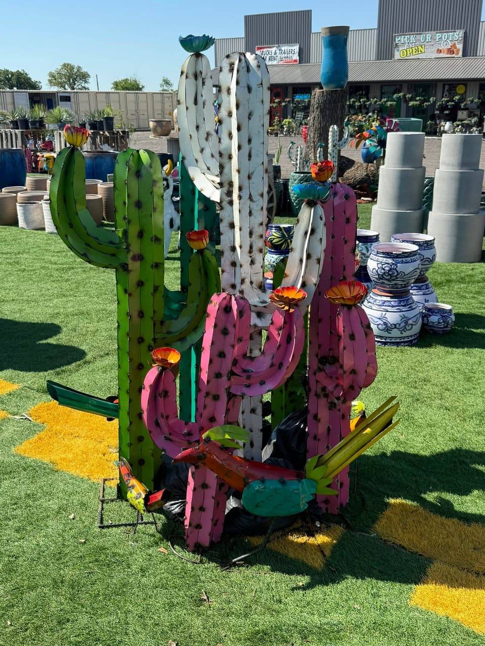 Tall painted metal saguaro cactus sculptures in green, white and pink with a metal roadrunner, beside Talavera-style pots at Pick Ur Pots in Stephenville