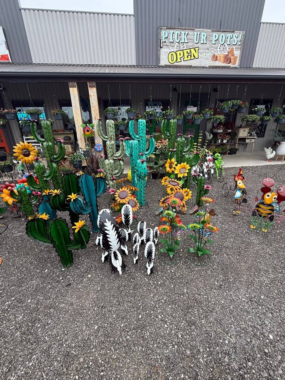 Metal cactus, sunflower, skunk and bee yard art on the gravel yard in front of the Pick Ur Pots storefront