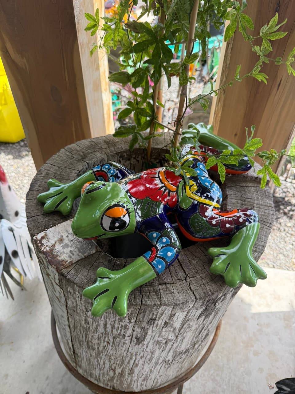 Hand-painted Talavera-style frog figure resting on a weathered wooden stump planter