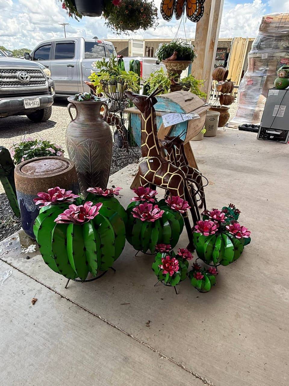 Metal barrel cactus art with pink flowers beside metal giraffes, a tall clay urn and a glazed fountain