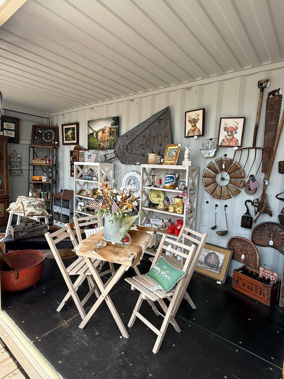 Antique booth with a folding table and chairs, a windmill wall piece, old farm tools, a cowhide and vintage tins