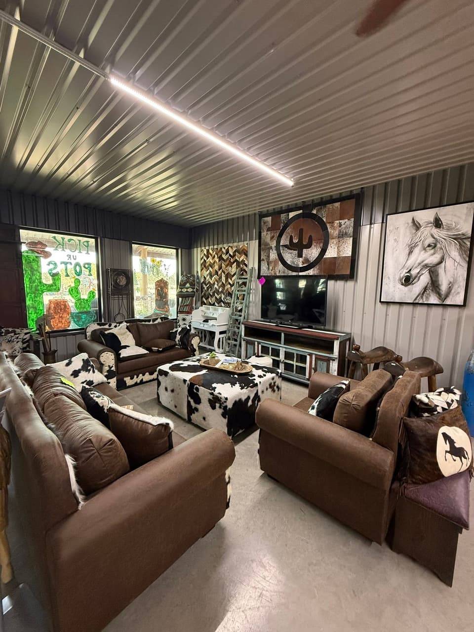 Western living room set with brown leather sofas, a cowhide ottoman, cowhide pillows, a cactus cowhide wall hanging and a horse painting at Pick Ur Pots in Stephenville, TX