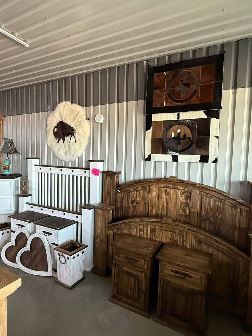 Rustic wood and white-painted bedroom furniture with arched headboards and nightstands, beside a buffalo sheepskin wall hanging and Texas and cactus cowhide patchwork art at Pick Ur Pots in Stephenville, TX